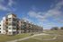 Modern multi-story apartment complex with expansive green lawns and clear blue skies.