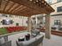 Modern apartment courtyard featuring cozy outdoor seating, vibrant red chairs on a lush lawn, and a large TV screen for communal entertainment under a stylish pergola.
