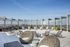 Luxurious rooftop terrace with modern wicker seating, sun loungers, and potted greenery under a clear blue sky.