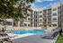 Modern apartment complex showcasing a luxurious pool area surrounded by stylish lounge chairs and lush greenery under a clear blue sky.
