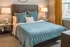 Cozy bedroom featuring a plush blue bedspread, elegant bedside tables with matching lamps, and stylish yellow curtains framing a sunlit window.