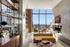 Luxurious modern living room with floor-to-ceiling windows offering stunning city views, stylish shelving, and elegant decor.