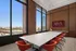 Elegant conference room with large windows offering a stunning cityscape view, featuring modern red seating and a sleek white table.