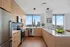 Modern kitchen with sleek cabinetry, stainless steel appliances, and stunning city skyline view through large windows.