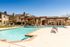 Luxurious apartment complex featuring a sparkling swimming pool surrounded by stylish seating and elegant wooden pergolas under a clear blue sky.