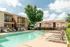 Inviting swimming pool area with sun loungers and modern apartment buildings, surrounded by lush greenery and clear blue skies.