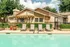 Inviting outdoor pool area with comfortable lounge chairs, surrounded by lush greenery and a charming house backdrop.