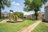 Charming apartment complex with lush greenery, featuring a vibrant playground under a clear blue sky, ideal for family living.
