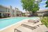 Inviting apartment community featuring a sparkling swimming pool with comfortable lounge chairs, set against charming two-story buildings and lush greenery.