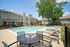 Inviting apartment community pool area with lounge chairs, patio seating, and lush greenery on a sunny day.