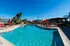 Inviting outdoor pool area with vibrant red lounge chairs and umbrellas, surrounded by lush greenery and clear blue skies.