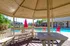 Charming gazebo with a view of a sunlit swimming pool and vibrant red umbrellas, perfect for outdoor relaxation and leisure.