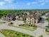 Charming residential community with elegant tan buildings, manicured landscaping, ample parking, and a pool, nestled in a serene green setting under blue skies.
