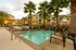 Luxurious apartment complex with a sparkling pool, surrounded by lush palm trees and elegant outdoor seating, perfect for relaxation.