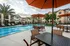 Inviting apartment community pool area featuring stylish lounge chairs, vibrant orange umbrellas, and lush palm trees under a beautiful sky.