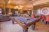 Luxurious lounge area featuring a sleek pool table, modern kitchen, and elegant dining space with vibrant red chairs in a stylish apartment.
