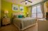 Inviting bedroom with a cozy atmosphere featuring a plush bed, stylish decor, vibrant green accent wall, and ample natural light from large windows.