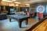 Luxurious recreation room with a sleek pool table, stylish seating, and a modern kitchen backdrop, perfect for entertainment and relaxation.