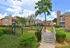 Charming apartment complex with lush green gardens, a quaint wooden bridge, and warm brick buildings under a bright blue sky.