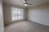 Bright and airy room with plush carpeting, large window providing ample natural light, and a modern ceiling fan.