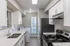 Modern kitchen with sleek white cabinetry, stainless steel appliances, and built-in washer and dryer, bathed in natural light from a large window.