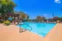 Inviting outdoor swimming pool with a charming pergola, surrounded by lush greenery and vibrant umbrellas under a clear blue sky.