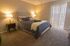 Cozy bedroom with a modern double bed, warm lighting, and floor-to-ceiling blinds inviting natural light.