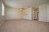 Inviting living room with plush carpet, neutral walls, and ceiling fan, leading to a quaint kitchen window and hallway.