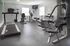 Modern fitness center with state-of-the-art equipment including treadmill, weight bench, and cardio machines in a bright, spacious room.