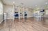 Bright and spacious open-plan area featuring sleek wooden floors, cozy workstations with blue chairs, and a stylish dining space with tall white chairs and lush greenery accents.
