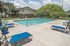 Inviting outdoor pool area with vibrant blue loungers, surrounded by lush greenery and a cozy two-story building, perfect for relaxation under a sunny sky.