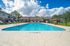 Inviting outdoor pool area with modern lounge chairs and vibrant potted plants under a bright blue sky, perfect for relaxation.