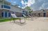 Inviting apartment complex with modern amenities, poolside loungers, and charming blue-accented balconies under a vibrant sky.