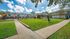 Charming apartment complex with lush green lawns, stylish pathways, and vibrant outdoor seating under bright orange umbrellas.