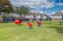 Inviting dog park with playful red agility equipment, lush green grass, and charming suburban homes in the background.