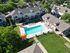 Charming apartment complex with a central pool, sun loungers, and vibrant orange umbrellas, nestled in lush greenery.