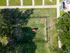 Aerial view of a vibrant green dog park with a central red agility tunnel, surrounded by lush trees and well-maintained pathways, offering a perfect outdoor experience.