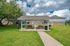 Charming outdoor picnic area with two red picnic tables under a covered shelter, surrounded by lush green grass and brick buildings, perfect for gatherings and relaxation.
