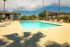 Inviting apartment complex with a sparkling outdoor swimming pool, surrounded by lounge chairs and palm trees, under a clear blue sky.