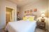 Inviting bedroom with plush bedding, vibrant artwork, cozy lighting, and a practical workspace, leading to a spacious walk-in closet.