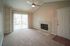 Inviting living room featuring plush carpet, a modern ceiling fan, and a cozy fireplace with natural light streaming through large sliding glass doors.