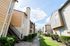 Charming apartment buildings with modern architecture nestled along a lush, green pathway under a bright, sunny sky.