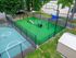 Vibrant outdoor recreational area featuring a pet agility course and a basketball half-court, surrounded by lush greenery and fencing.