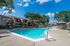 Inviting apartment complex pool area with surrounding lounge chairs, vibrant umbrellas, and lush greenery on a sunny day.