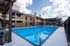 Inviting apartment complex featuring a sparkling swimming pool with lounge chairs and shaded seating area, surrounded by charming brick buildings under a bright, blue sky.