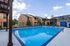 Inviting apartment complex with a sparkling blue swimming pool, surrounded by elegant brick buildings and outdoor lounging area under a clear, sunny sky.