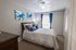 Cozy bedroom with soft lighting, featuring a plush bed adorned with blue and purple pillows, elegant wall art, and vibrant blue curtains.