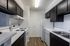 Modern kitchen with sleek dark cabinets, white countertops, and wood flooring, featuring essential appliances.