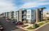 Modern apartment complex with sleek architecture, large windows, and ample parking under a clear blue sky.