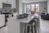 Modern open-plan kitchen with sleek white cabinetry, stainless steel appliances, and a stylish breakfast bar with metal stools, offering a cozy view into the sunlit living area.